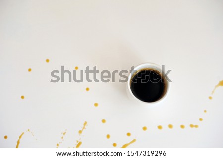 Cup of espresso on a white surface splattered with drops of coffee. Background, free space for text