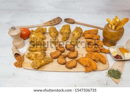 Chicken wings, home made fried food, fast food products: onion rings, chicken wings, french fries, fried chicken on a wooden plate.