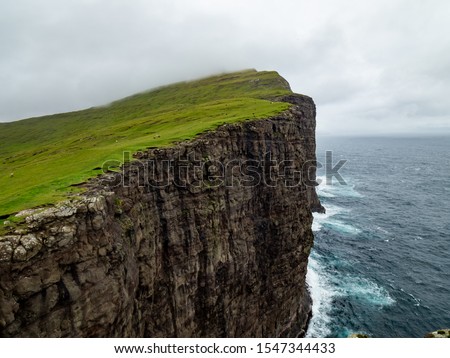 Steep cliffs of Faroe Islands. Green grass at the top, Ocean below the cliffs.  Royalty-Free Stock Photo #1547344433