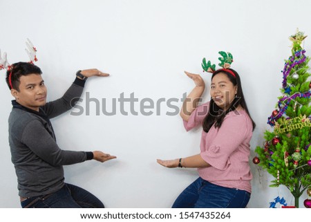 loving asian couple man and woman  with christmas tree and cute bandana hand point on empty space.  Christmas, New Year, Valentine day, holiday, people - concept.
