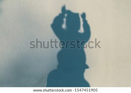 The contour of the figure of child expressively raising both hands up above his head, drawn by a sunny shadow on the textured wall of the building. Halloween background.