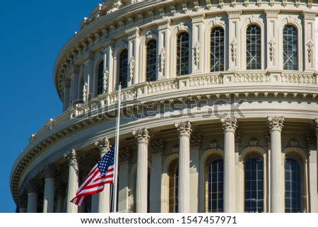 A close up of U.S. Capitol Building  with American flag flown at half-staff in the wind. 