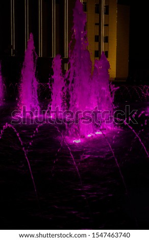 Pink fountain shot at night. Silhouettes of people on a background of water from a fountain.