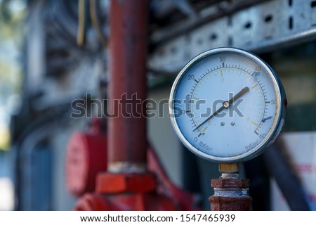 Small industrial analoge pressure guage, with out of focus pipes in the background