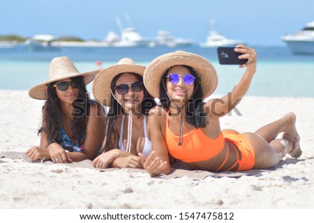 Three happy girls friends in summer clothes taking a selfie at the beach