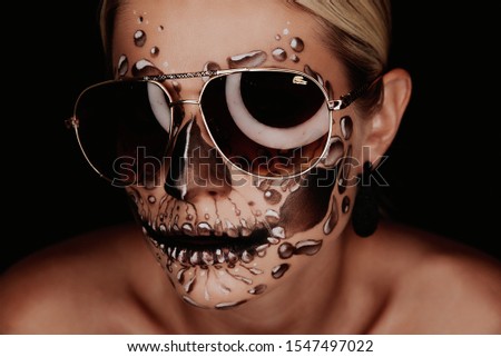 Portrait of a woman with sugar skull makeup over red background. 
girl with glasses for halloween.
Halloween costume and make-up.  Royalty-Free Stock Photo #1547497022