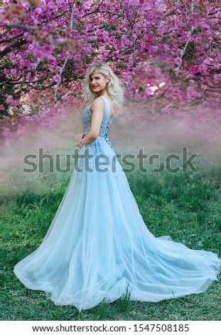 An incredible, delicate blonde in a luxurious, delicately blue dress walks in the spring, sakura and cherry orchards are in bloom. Princess with long curly hair. Vanilla color art photo Royalty-Free Stock Photo #1547508185