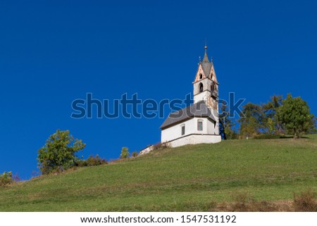 Church of Santa Barbara on a hill with blue sky background in LaVall Tolpei in the Italian Dolomites.
