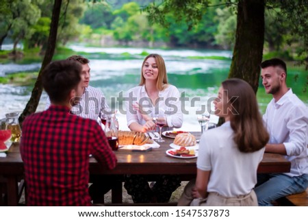 group of happy friends having picnic french dinner party outdoor during summer holiday vacation  near the river at beautiful nature
