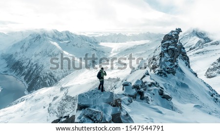 Traveler contemplates snowy mountain landscape. Man stay above heavy mist in deep valley. Hike in pure nature is the popular recreation activity in all of the world.