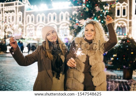 Picture of two women with Bengal lights on winter walk on background of decorated spruce