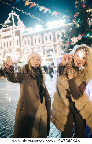 Picture of two women with Bengal lights on winter walk on background of decorated spruce
