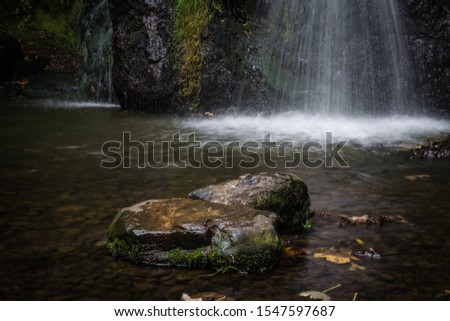 A stone in the foreground with a waterfall in the background in the Fairy Glen Falls, Rosemarkie, Fortrose, Highlands, Scoland, United Kingdom