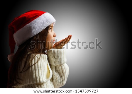 Merry Christmas and happy holidays! Cute little child girl with xmas present. Santa Kid enjoy the holiday. Portrait kid with gift on dark background.
