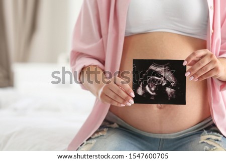 Pregnant woman with ultrasound picture indoors, closeup