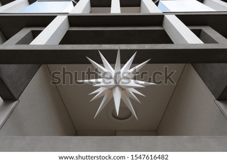 Architectural monochrome geometric shapes. White peaky 3D figure between grey squared walls. Star shaped lampshade closeup. Minimal Christmas balcony decoration. Unusual background. Geometric backdrop