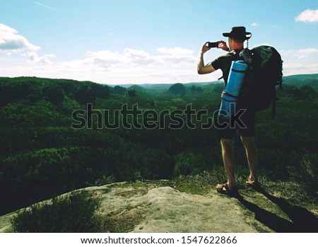 Backpacker man taking selfie picture using smartphone during walking by hot foggy weather mountain range