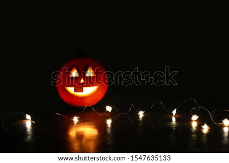 Curved orange pumpkin jack-o-lantern in the darkness surrounded by ghost lights with a place for text on black background. Halloween decoration.