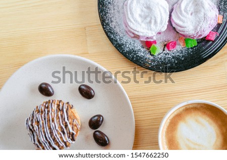 Sweet tasty pastries covered with sugar powder and glazed on plates with a cup of cappuccino  on a wooden background top view. Spase for text. Background. Closeup