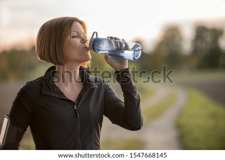 Young woman drinking water during sports outside in the nature