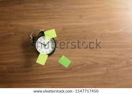 Alarm clock and empty sticky notes on wooden table top.