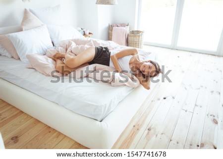 Tender bedclothes. Cute girl keeping smile on her face while spending morning in her bedroom