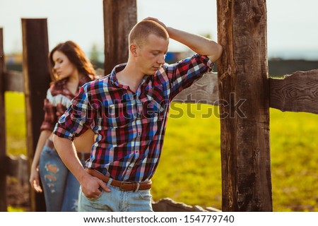 young adult couple on the farm standing near fence, man in the foreground