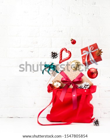 Christmas shopping. Magic concept. Red cotton bag with gift boxes, candy and other New Year decorations fly or fall on white background.