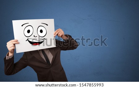 Young student holding a paper with laughing emoticon in front of his face