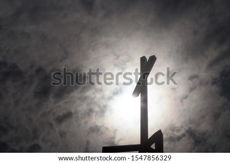A Christian crucifix atop a church silhouetted by rays of light from above.