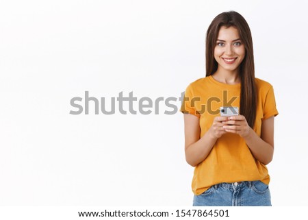 Sassy, happy good-looking woman in yellow t-shirt, holding smartphone look camera pleased and cheerful, shopping online, download mobile application to edit photo and post social-network