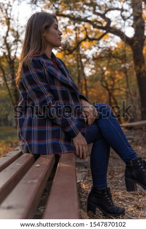 A beautiful Caucasian model enjoying an autumn walk, sitting on a bench in the park, a woman wearing a checkered coat