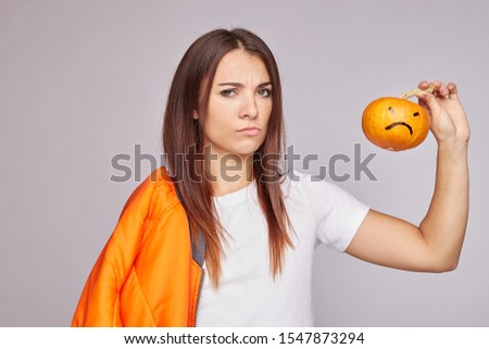 Close up portrait of young mixed raced woman feels disgust, holds small pumpkin, has dissatisfied facial expression, dressed in casual outfit, isolated over grey studio background. Facial expressions.
