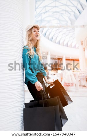 Black Friday. Discounts. Sales. Shopping A girl with packages and shopping smiles and enjoys new clothes. Black paper bags in hands on a blurred background of a shopping center.