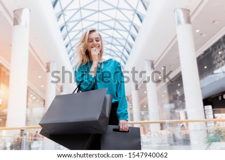 Black Friday. Discounts. Sales. Shopping A girl with packages and shopping smiles and enjoys new clothes. Black paper bags in hands on a blurred background of a shopping center.