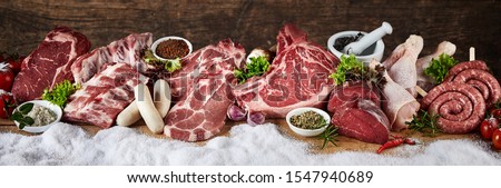 Large selection of prime raw meat for a winter BBQ in a panorama with pork, beef, chicken, steak and sausages in a row on snow with fresh herbs and spices suitable for butchery advertising Royalty-Free Stock Photo #1547940689