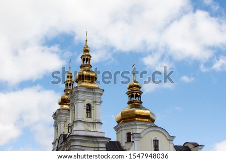 Golden domes with crosses of an orthodox temple on the background of bright blue sky. Snow-white facade. Christian faith.