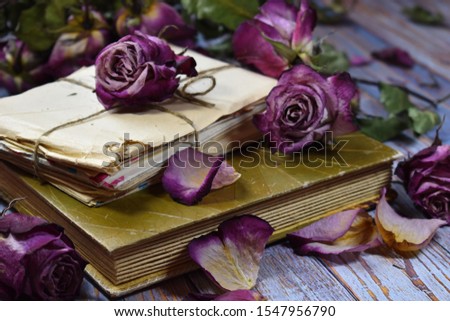 Nostalgic vintage mood background. Dry decorative purple rosebuds and old letters. Withered roses on an album close-up. Dying flowers, old letters and a photo album on the table. Memories of  past.