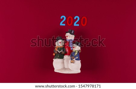 three toy snowmen, 2020 on a red background, Christmas background.