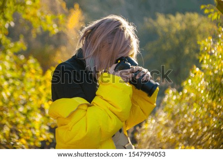 Young girl in yellow coat make photo with camera in the mountains. Sunny autumn day