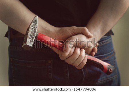 A man holds a hammer in his hands behind his back Royalty-Free Stock Photo #1547994086