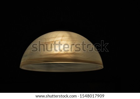 Beautiful silhouette of a pendant ceiling lamp in an isolated dark scene.  
Beautiful abstract contrast - the black background and the warm soft light of the bulb through the matte glass material.