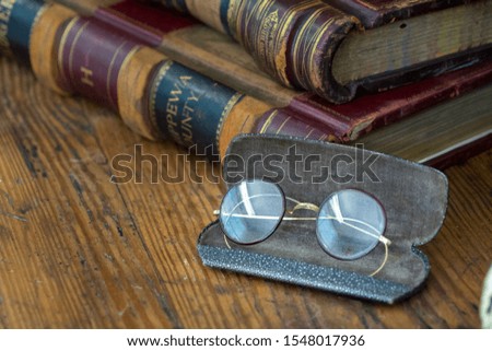 Antique glasses next to older books on a worn wooden desk