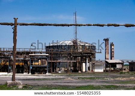 Old rusted oil tanks and pipe on soviet factory or plant. Blue sky background.