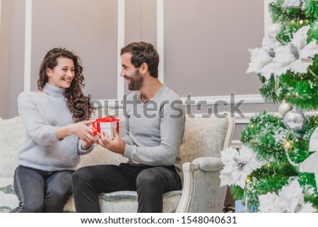 Image of affectionate girl giving present her boyfriend while sitting on the sofa in new year time.