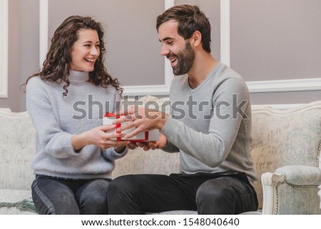 Image of affectionate guy giving present his girlfriend while sitting on the sofa in new year time.