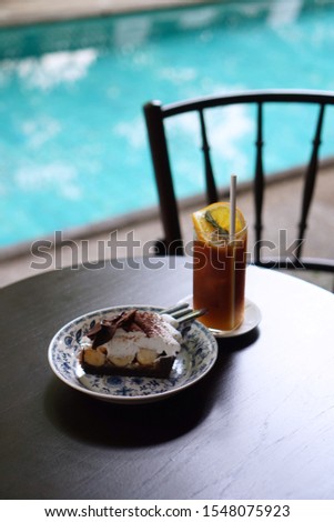 Ice tea lemon and Banoffee cake on wooden table beside swimming pool in cafe shop