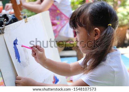 Close up of Asian child girl is holding paintbrush and painting on white paper. Selective focus