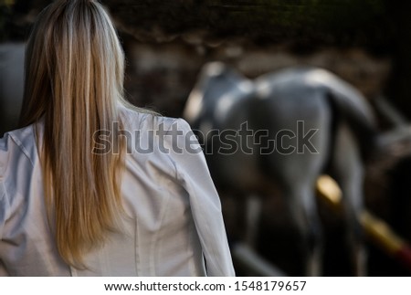 photo long-haired girl in a suit stands with his back to the head of a horse gray background