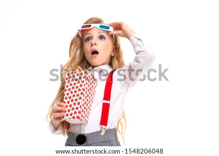 Small caucasian girl with makeup and long blonde hair with pop-corn and 3D glasses is shocked